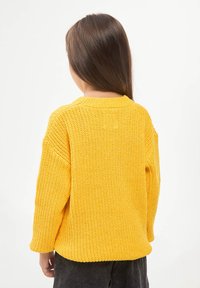 Maglione giallo a maglia con vestibilità ampia, tessuto texturizzato e polsini a coste. Termina all'anca con un colletto rotondo.