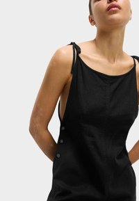 Abito nero senza maniche con spalline regolabili, dettagli con bottoni laterali e silhouette aderente, realizzato in un tessuto liscio.