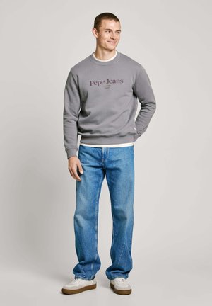 Sudadera gris con el logo "Pepe Jeans", combinada con jeans de color azul claro. Las zapatillas tienen una parte superior blanca y una suela marrón. Diseño simple y casual.