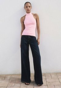Fitted pink halter top paired with wide-leg dark denim jeans. The outfit features a smooth texture and minimalist design.