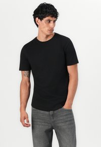 Black short-sleeve t-shirt in a fitted design, made of cotton, with a crew neckline and smooth texture. Paired with light gray jeans.