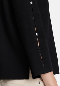 Czarny sweter dzianinowy z rękawami ozdobionymi guzikami i rozcięciami. Miękka tekstura, dopasowany krój i czyste linie.