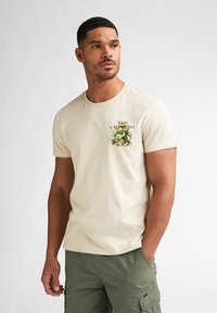 Beiges Baumwoll-T-Shirt mit kurzen Ärmeln und rundem Ausschnitt, versehen mit einem grünen Kaktus-Motiv und dem Schriftzug "BAJA CALIFORNIA" auf der linken Brust.
