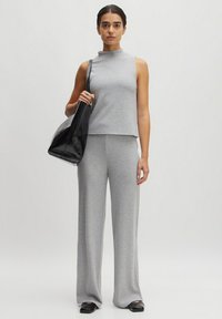 Gray ribbed tank top with high neck paired with matching wide-leg pants. Holds a black shiny bag. Flat black shoes, minimalist design.