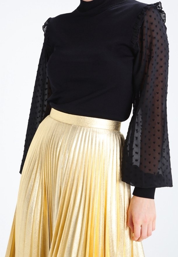 Top negro con mangas abullonadas transparentes y con estampado, combinado con una falda plisada dorada metálica de cintura alta.