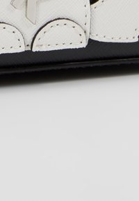 Zwarte handtas met een gestructureerd oppervlak, witte leren accenten, een zilveren logo en afgeronde randen met contrasterende stiksels.