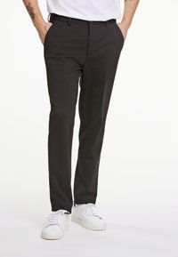 Schwarze maßgeschneiderte Hose mit glatter Textur, geradem Schnitt, subtiler Falte und slim fit, kombiniert mit weißen Sneakers.