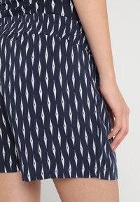 Marineblauwe shorts met een diamantpatroon in wit en lichtblauw. Gemaakt van zachte stof, met een elastische tailleband en zijzakken.