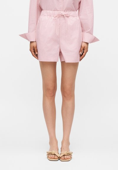 Femme portant un short rayé rose clair avec une taille élastique et un lien, associé à une chemise à manches longues assortie et des sandales beiges à enfiler.