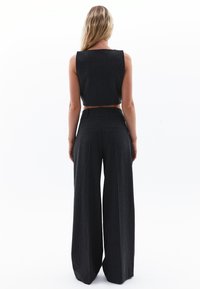 Crop top a righe grigio scuro e pantaloni a gamba larga. Il tessuto ha una consistenza morbida. Vestibilità su misura con vita alta e tasche posteriori.