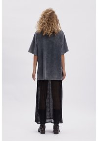 Overdimensioneret grå bomulds t-shirt med et falmet udseende, parret med en gennemsigtig sort strikket maxi-nederdel. Begge beklædningsgenstande har afslappede silhuetter.