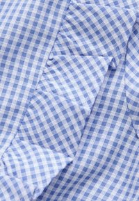 Blauw-witte ruitjesstof met een gerimpelde rand, met zichtbare textuur en vouwdetails.