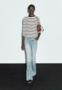 Gestreepte langemouwen top in crème en zwart, gecombineerd met lichtblauwe flare jeans. Accessoires zijn een bruine handtas en een zwarte sjaal.