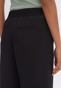 Svarta byxor med en avslappnad passform, med elastisk midja och en enda bakficka. Slät textur och minimala designdetaljer.