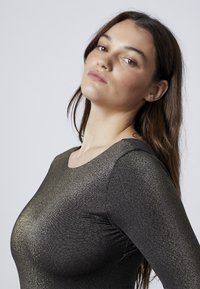 Top nero a maniche lunghe con una texture metallizzata liscia e una finitura lucida. Collo rotondo, design aderente e una leggera lucentezza.