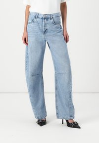 Lyseblå vide jeans med høy midje, med klassisk femlommesdesign og subtile sømdetaljer. Brukt med svarte spisse hæler.