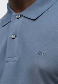 Gaiši zils polo krekls no teksturēta auduma, ar apkakli, diviem pogām un priekšpusē ieembosētu logotipu "BOSS".