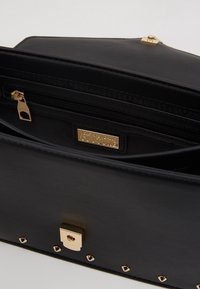 Clutch in pelle nera con zip e lucchetto dorati, etichetta interna che recita "Versace Jeans Couture," e abbellimenti a borchie dorate sulla parte anteriore.