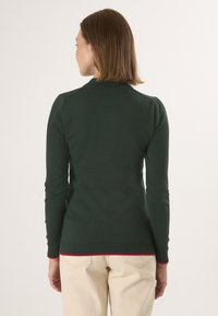 Groene gebreide trui met lange mouwen, geribde manchetten en een rode accent aan de zoom, met een gladde textuur en een aansluitend ontwerp.