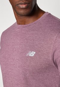 T-shirt à manches courtes et col rond en tissu violet chiné avec une texture lisse. Présente un logo "NB" blanc sur la poitrine gauche.