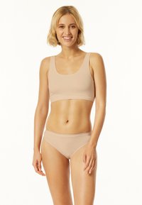 Béžová podprsenka a bikini set vyrobené z hladké tkaniny. Vrchní část má kulatý výstřih a široká ramínka, zatímco bikini mají nízký střih.