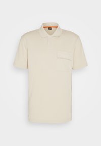 Polo shirt beige à manches courtes en tissu doux, avec un col classique, trois boutons et une poche sur la poitrine.