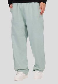 Világoszöld, kényelmes szabású melegítőnadrág puha anyagból, rugalmas derékpánttal és oldalzsebekkel, fehér tornacipővel párosítva.