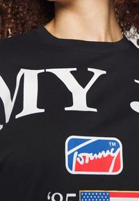 Black cotton T-shirt with bold white text "MY" and a colorful logo. Features a round neck and smooth texture, ideal for casual wear.