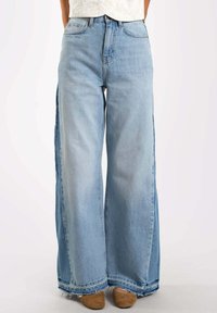 Jeans de mezclilla azul claro, de pierna ancha, con dobladillo deshilachado y aberturas laterales. Presentan un diseño clásico de cinco bolsillos y trabillas para cinturón.