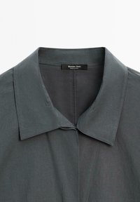 Camicia collare grigia scura con colletto ampio e appuntito e con un'etichetta di marca visibile all'interno del colletto.