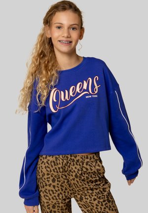 Blauwe cropped sweatshirt met de tekst "Queens" in oranje en wit, gecombineerd met braune luipaardprint broek met een elastische tailleband.