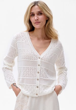 Witte gebreide cardigan met een V-hals, voorzien van een openwerk patroon, geribbelde randen en knopen aan de voorkant. Lange mouwen en een lichte textuur.