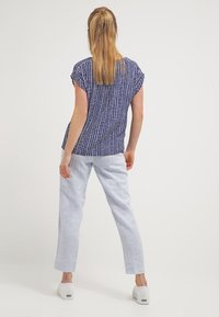 Marinblå mönstrad kortärmad topp med rutmönster, kombinerad med ljusblå linnebyxor med rak passform och vita skor. Bakifrån visad.