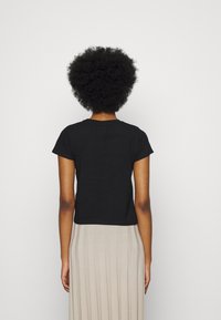 T-shirt nera a maniche corte con collo rotondo, realizzata in cotone, abbinata a una gonna beige plissè. La vista dal retro mostra una vestibilità rilassata e una texture liscia.