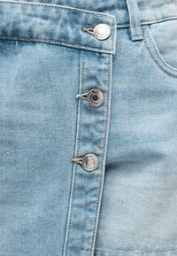 Ανοιχτό μπλε ύφασμα τζιν με τρία ασημί μεταλλικά κουμπιά στερεωμένα σε κάθετη σειρά σε ένα ρούχο.