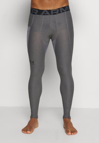Leggings de sport gris avec une finition texturée, dotés d'une taille noire, de panneaux latéraux gris clair et d'un logo contrastant sur la jambe inférieure.