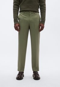 Skræddersyede bukser i olivengrøn med en glat finish, der har bæltestropper og rette ben, kombineret med mørkebrune sko.