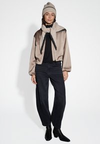 Giacca bomber cropped beige satin, top nero a costine, jeans neri a vita alta, sciarpa beige con bordo scuro e berretto lavorato a maglia beige.