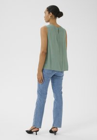 Ärmlös grön topp med en nyckelhålsdetalj på ryggen, i kombination med ljusbl�å raka jeans och svarta spetsiga klackar.