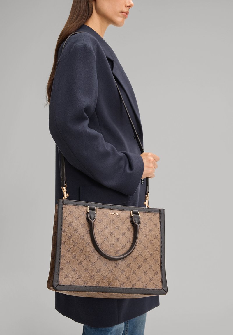 Bolso tote con estampado marrón, ribete de cuero negro, dos asas superiores y una correa de hombro desmontable, mostrado sobre un fondo neutro.