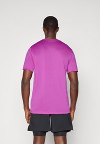 Lila sportliches T-Shirt mit kurzen Ärmeln, taillierter Passform, glatter Textur und minimaler Nahtgestaltung, kombiniert mit schwarzen Shorts.