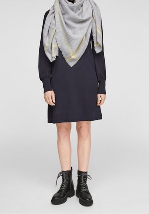 Robe en tricot bleu marine à manches longues, associée à une écharpe gris clair avec des rayures jaunes. Des bottes de combat noires à lacets complètent le look.