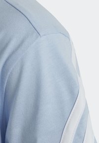 Ljusblå bomulls T-shirt med ribbat mönster, insydd ärmdesign och vita accentränder längs axlarna.