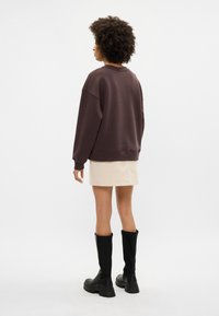 Sweatshirt oversized castanho, saia bege e botas pretas até ao joelho. Tecido suave com um corte descontraído e ombros caídos. Design simples.
