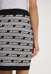 Gonna in maglia con una fantasia a righe bianche e nere, caratterizzata da testo ripetuto "JEANS" e "JOOP!" in grassetto. Vita alta con una texture liscia.
