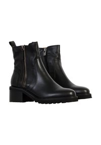 Botas de cuero negro hasta el tobillo con un tacón grueso, cremalleras laterales y suelas de goma texturizada para mayor agarre, con un diseño minimalista.