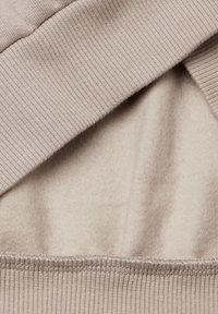Tessuto beige chiaro, caratterizzato da una superficie liscia e morbida con accenti a coste lungo i bordi. Sono visibili due strati, uno soffice e uno piatto.