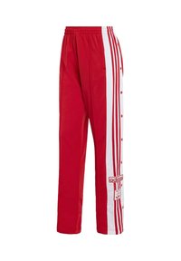 Červené atletické nohavice vyrobené z hladkého materiálu, so bielymi bočnými pruhmi, cvokmi a vyšitým logom na prednej strane.