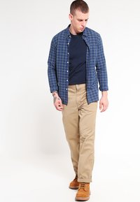 Blauw geruit overhemd over een marineblauw T-shirt, gecombineerd met kaki broeken en tan laarzen, met een ontspannen pasvorm en middelgewicht stof.