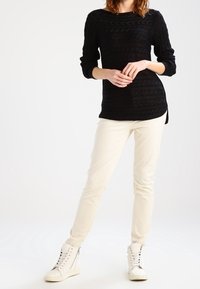 Svart texturerad stickad topp med långa ärmar, ihop med vita slim-fit byxor och vita högstamsneakers.